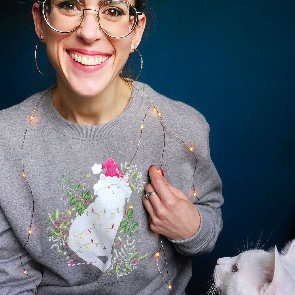 Smiling lady in glasses wearing a grey christmas jumper with white cat